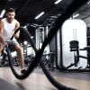 Athletic young man with battle rope doing exercise in functional training fitness gym.