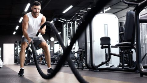 Athletic young man with battle rope doing exercise in functional training fitness gym.
